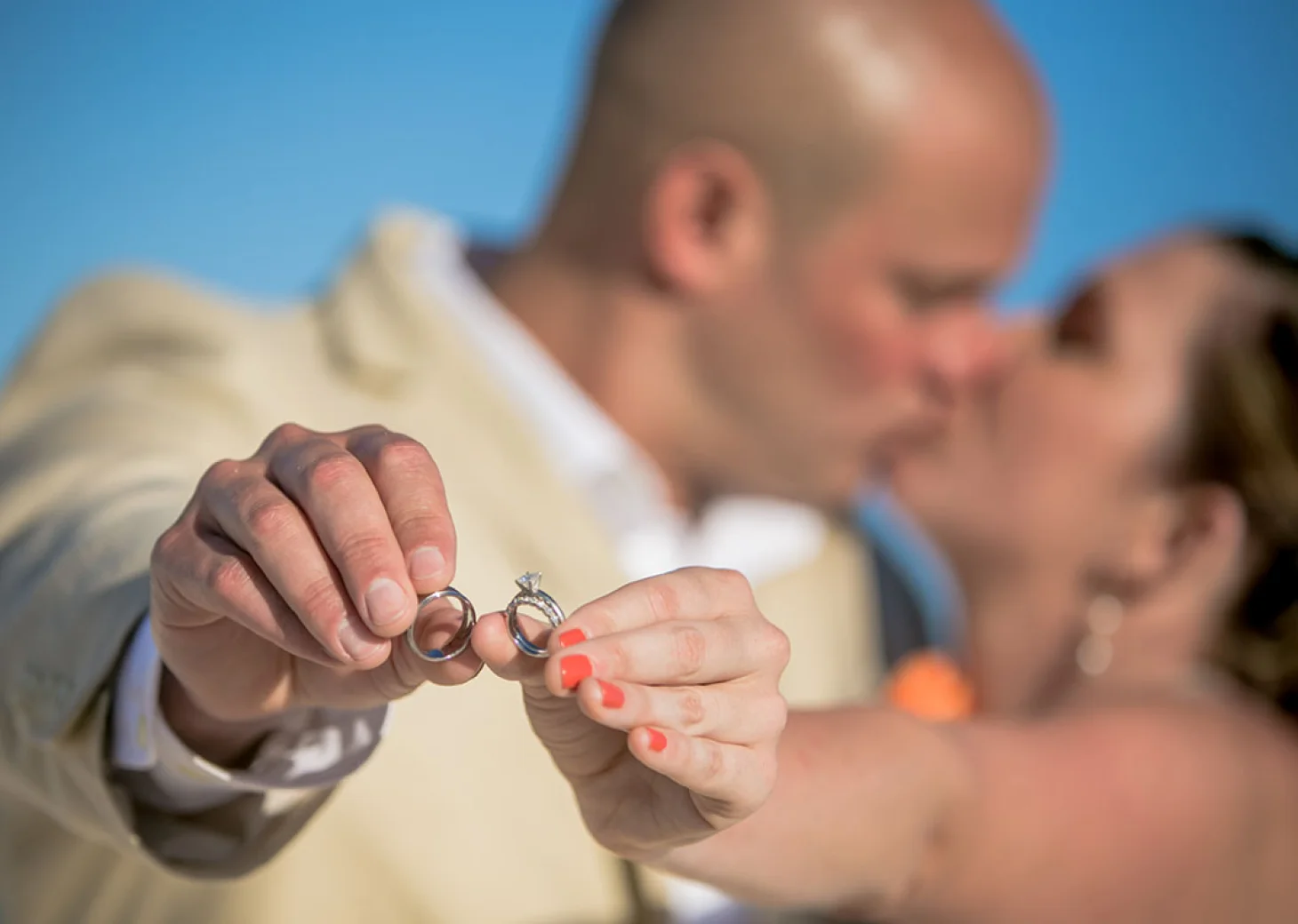 Bride and Groom showing their wedding bands while kissing on background.