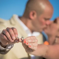 Bride and Groom showing their wedding bands while kissing on background.