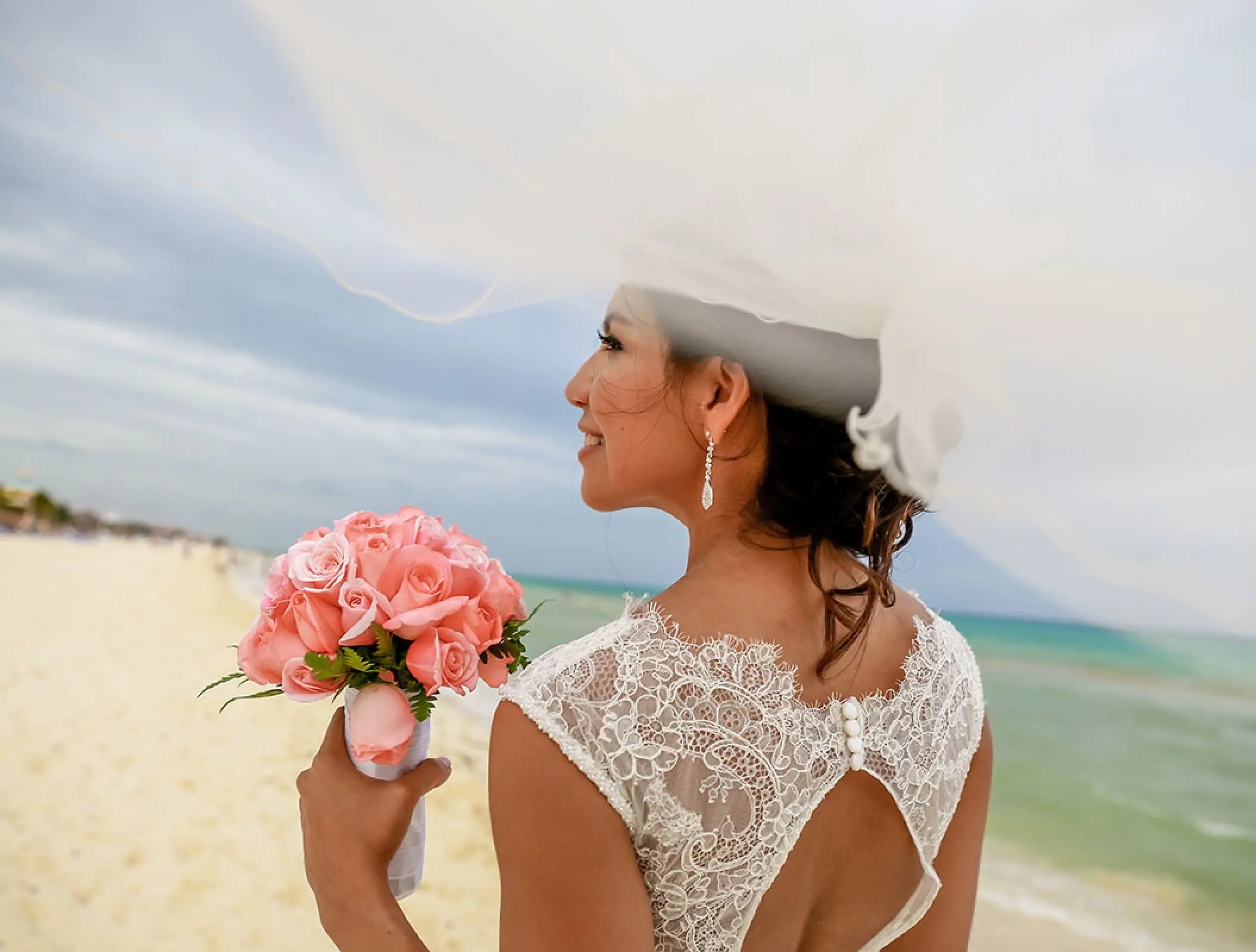 Bride in a lace dress holding a pink rose bouquet at Hilton Tulum