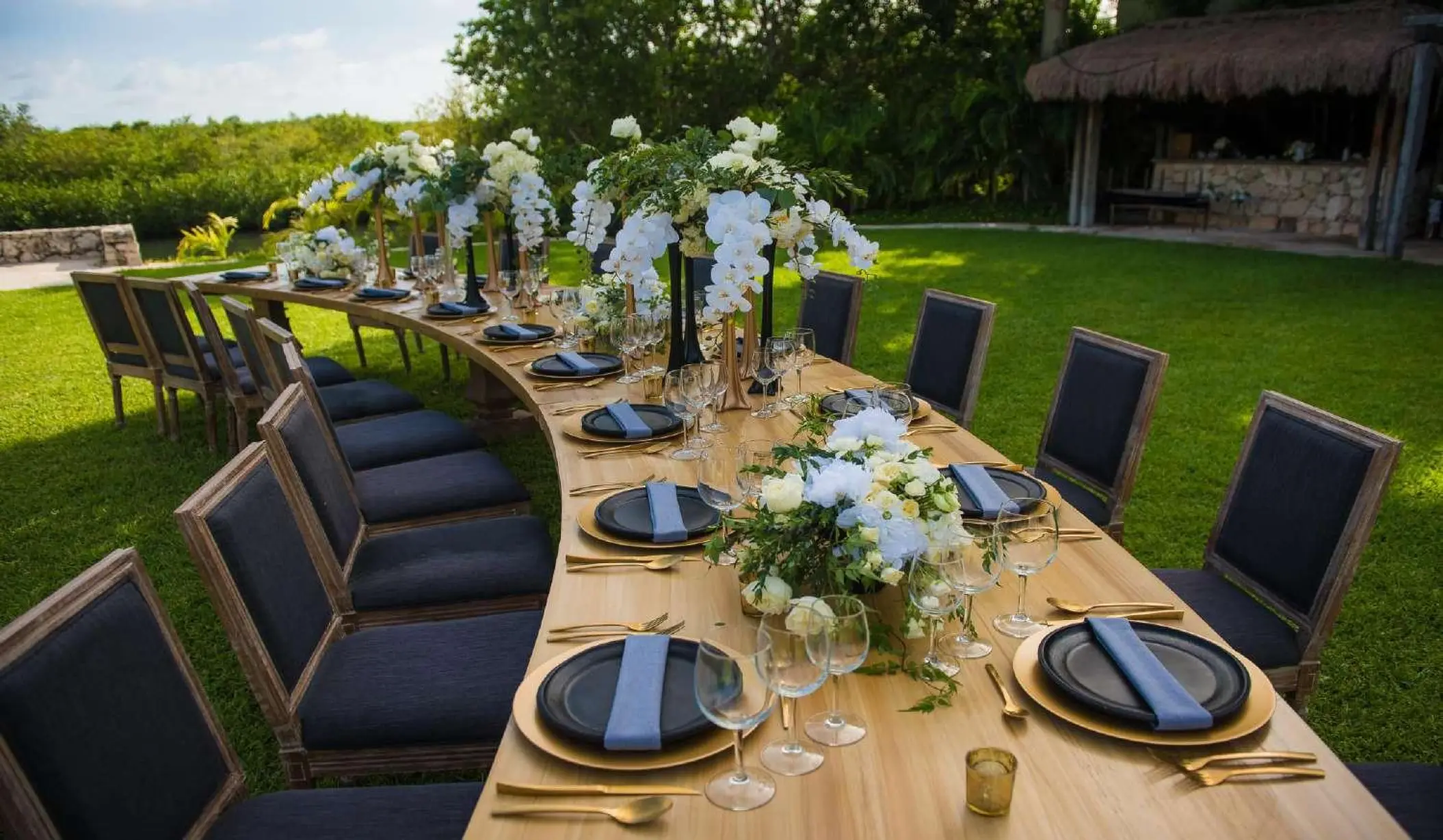 Curved wooden wedding reception table with white floral centerpieces on the lawn at Nizuc Resort, Cancun