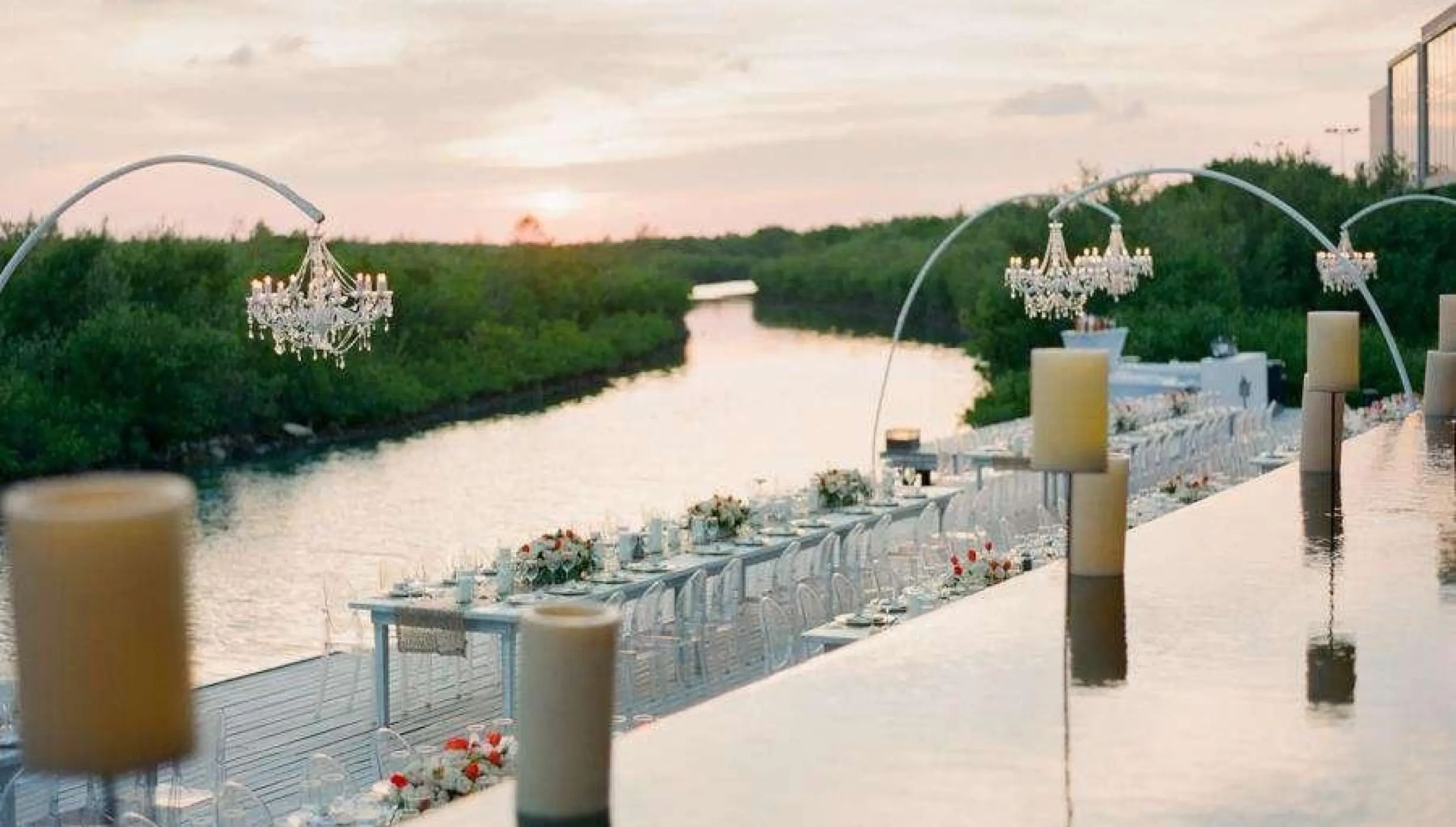 Outdoor wedding reception at Nizuc Resort, Cancun featuring chandeliers over a terrace by the water at sunset