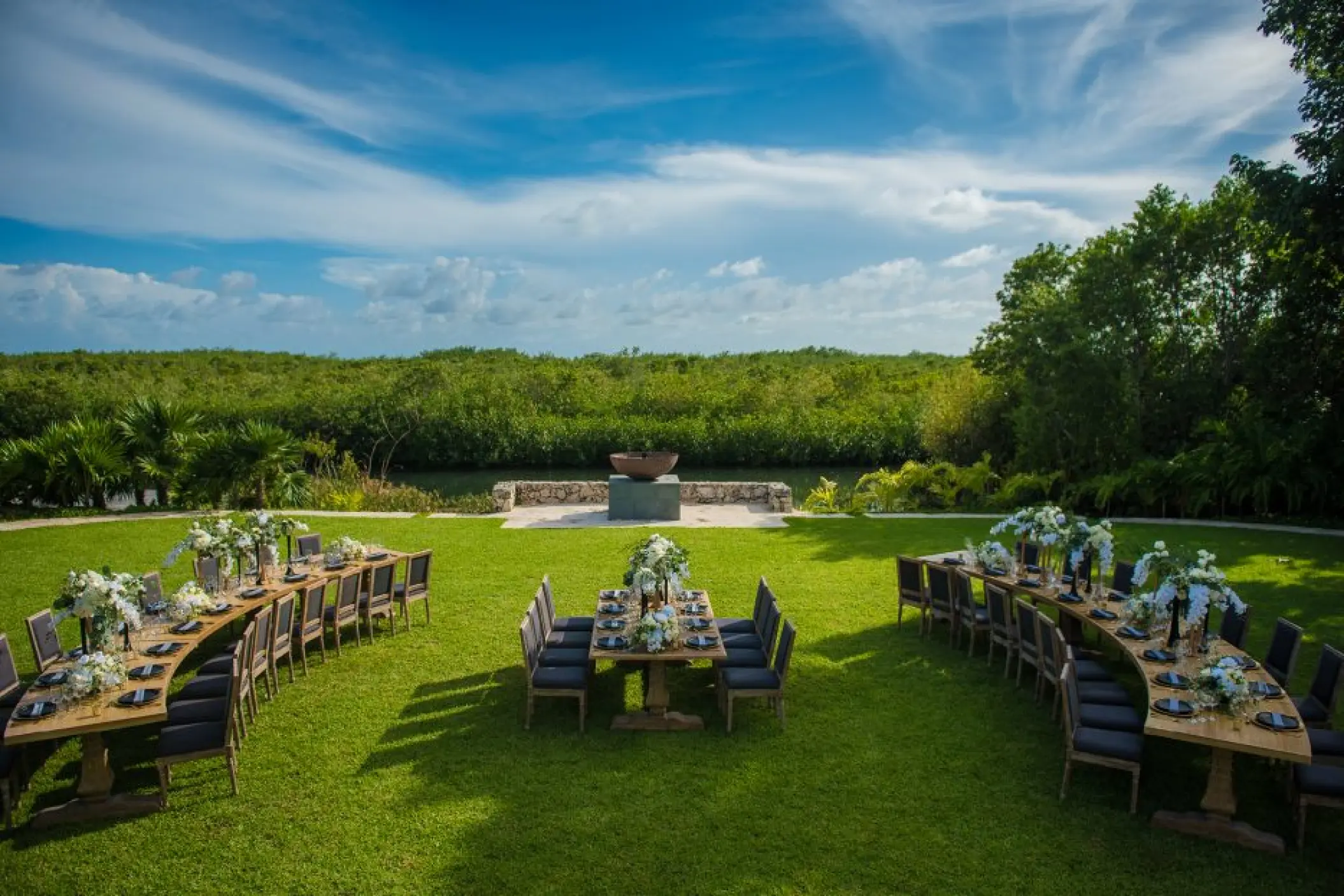 Outdoor wedding reception with curved wooden tables on a green lawn at Nizuc Resort, Cancun