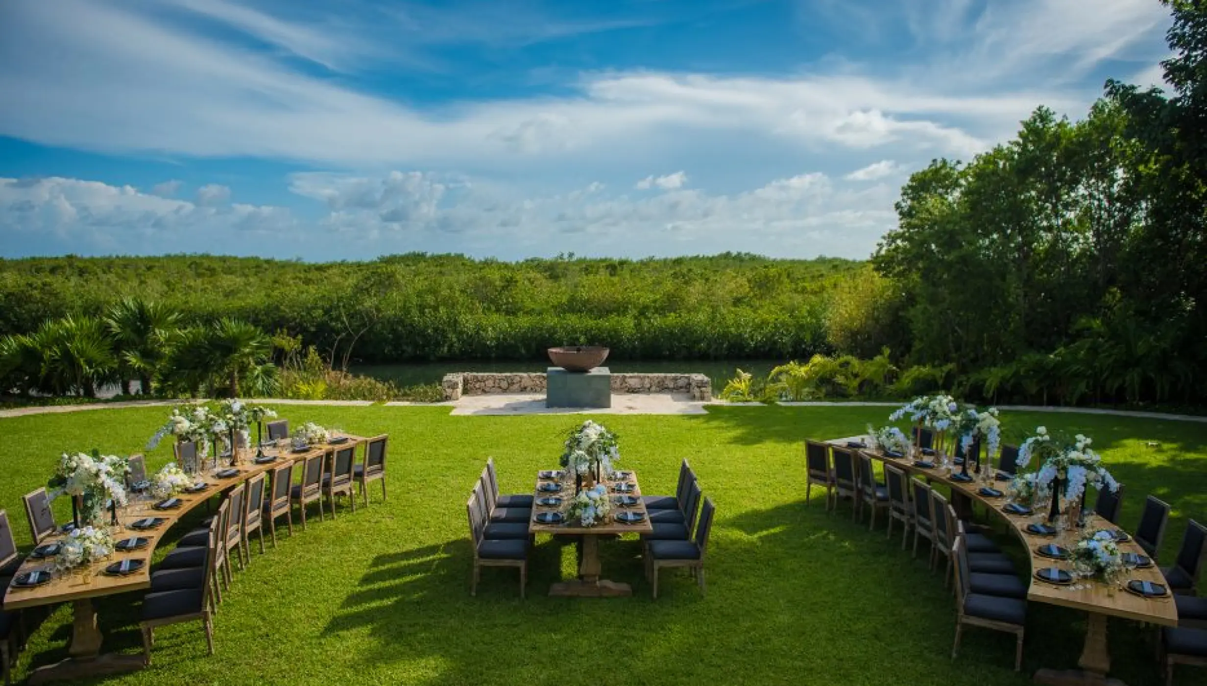 Outdoor wedding reception with curved wooden tables on a green lawn at Nizuc Resort, Cancun