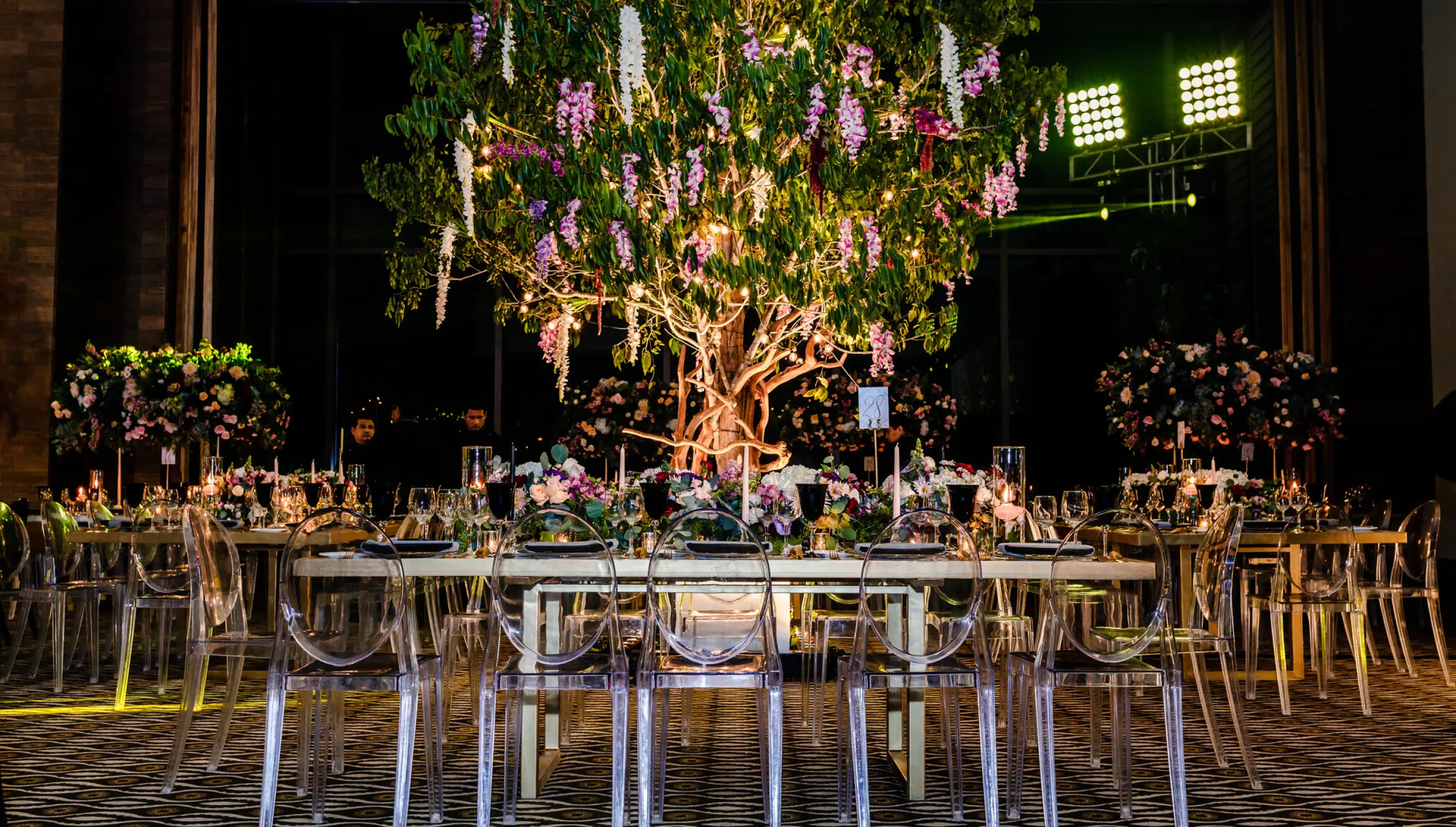 Indoor wedding reception with clear chairs and a large lit tree centerpiece at Nizuc Resort, Cancun