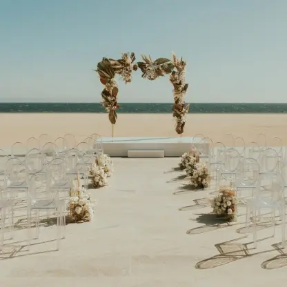 Beachfront wedding ceremony with clear chairs and a dried floral arch at Nobu Los Cabos, Cabo San Lucas