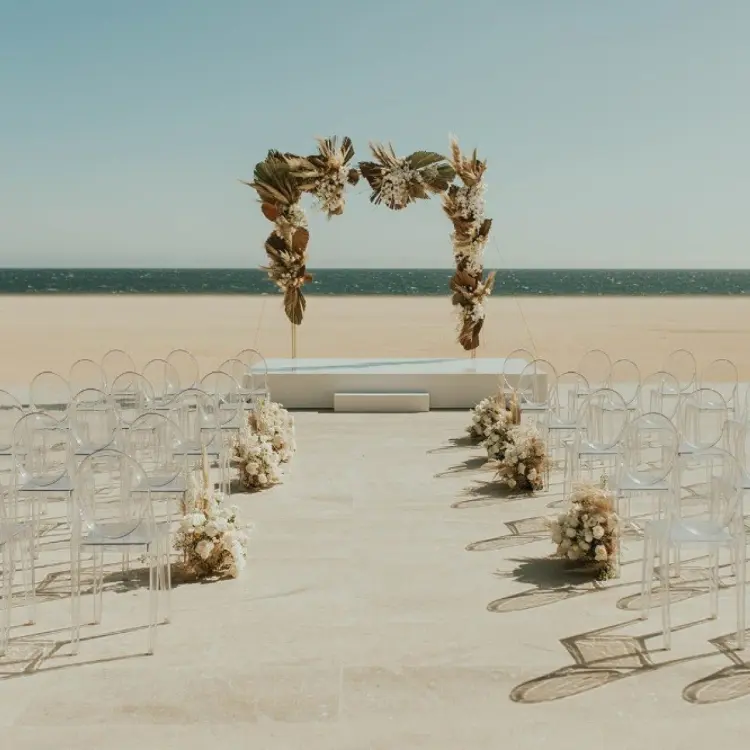 Beachfront wedding ceremony with clear chairs and a dried floral arch at Nobu Los Cabos, Cabo San Lucas