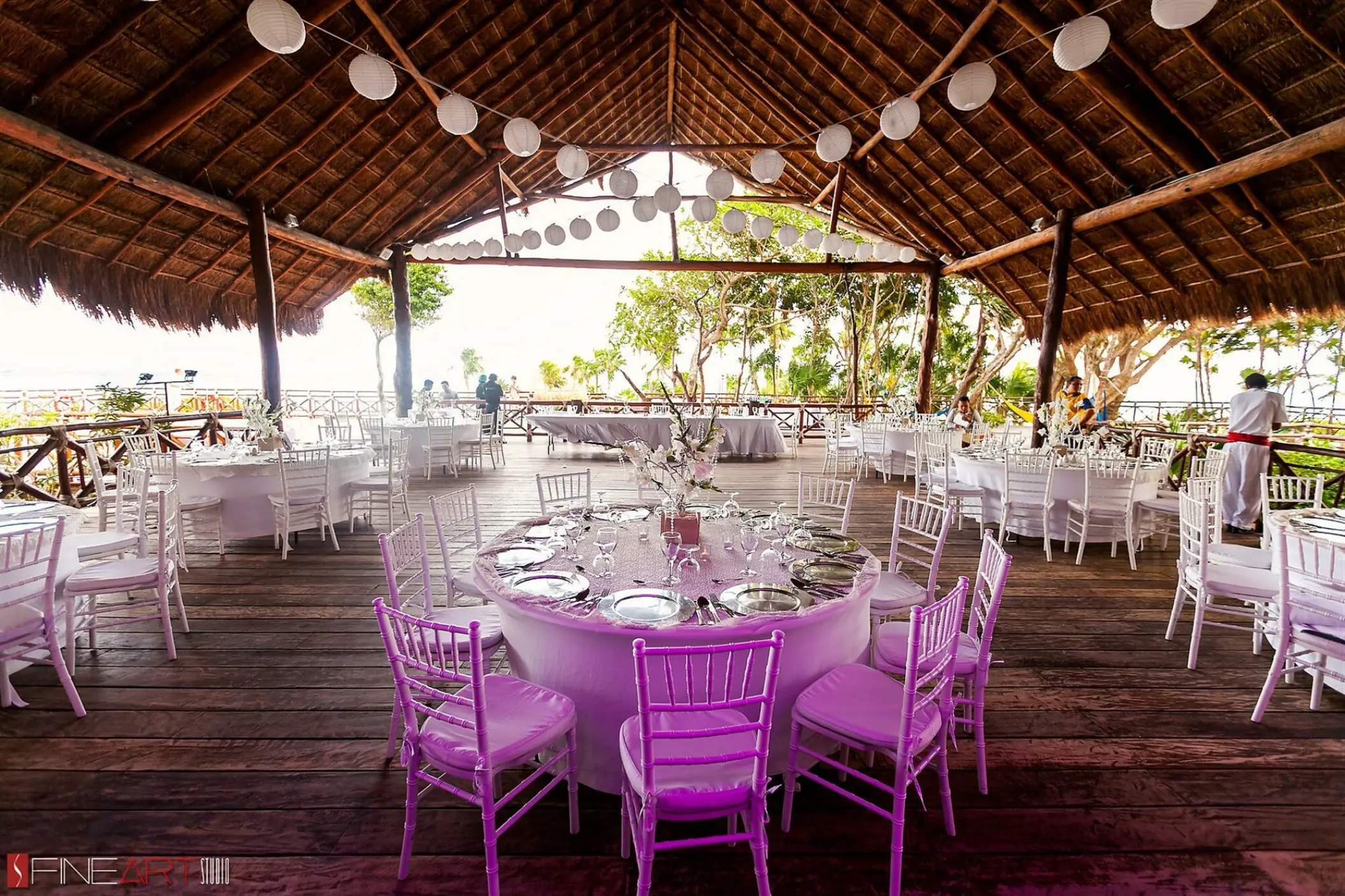Palapa wedding reception with round tables and white paper lanterns at Occidental at Xcaret, Playa Del Carmen