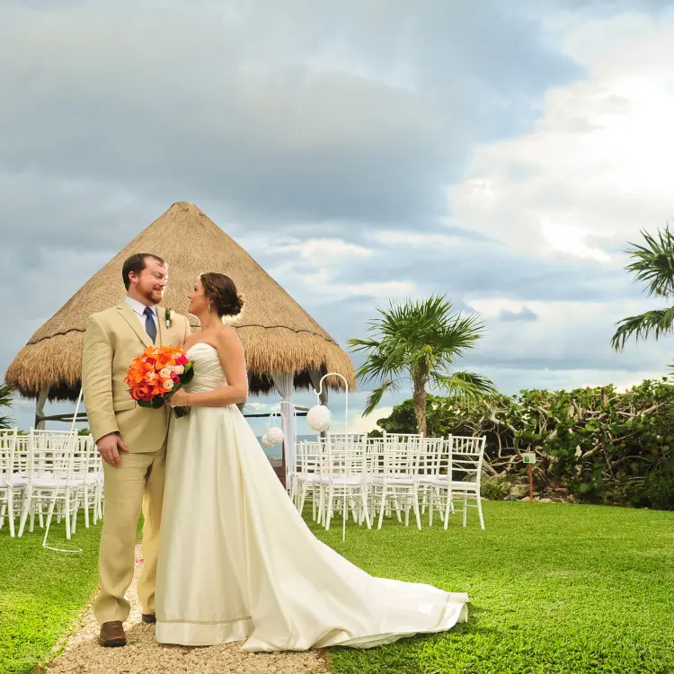 The bride and groom standing before a palapa wedding ceremony venue at Occidental at Xcaret, Playa Del Carmen