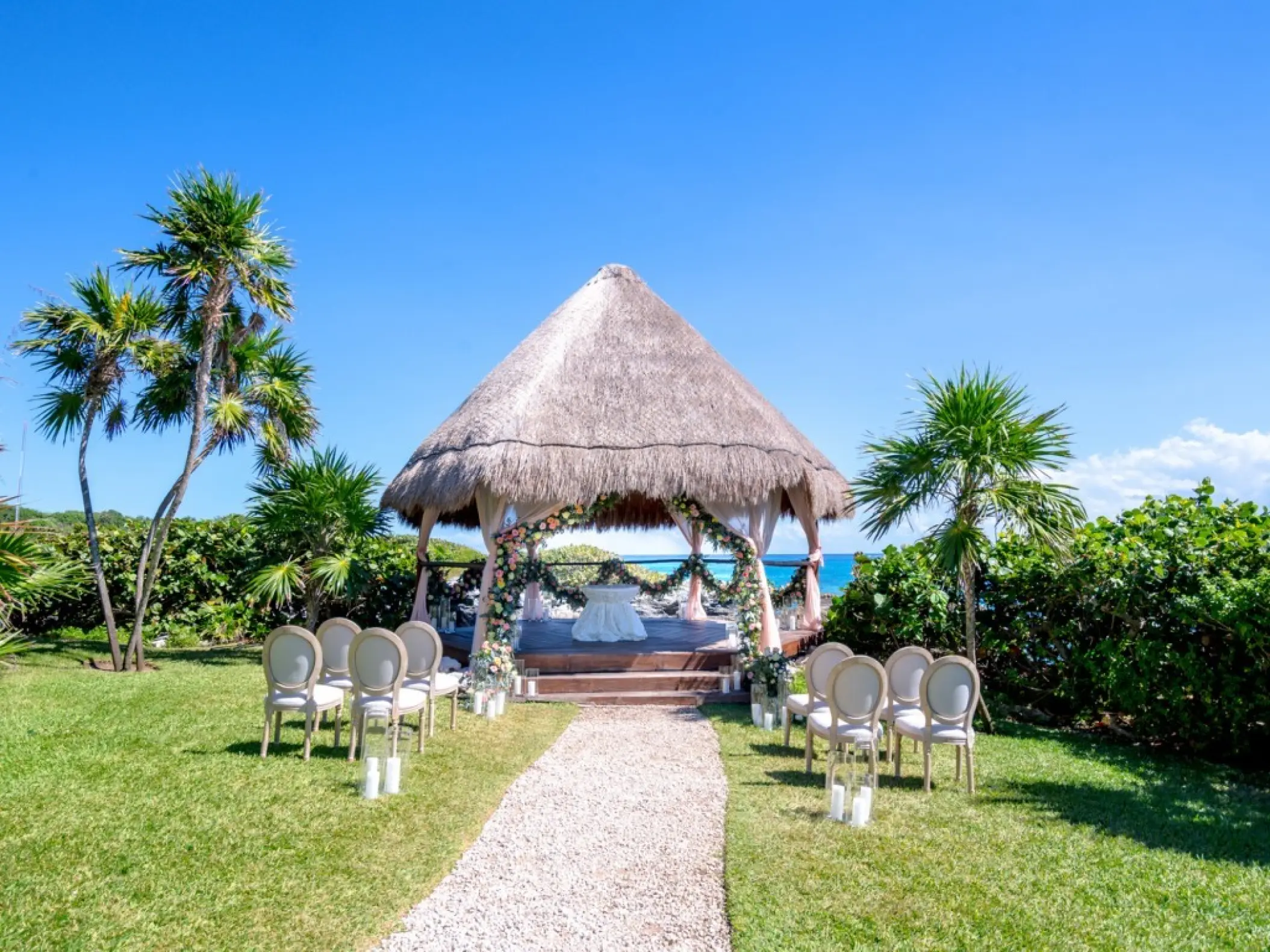 Palapa wedding ceremony with a floral arch and white chairs at Occidental at Xcaret, Playa Del Carmen