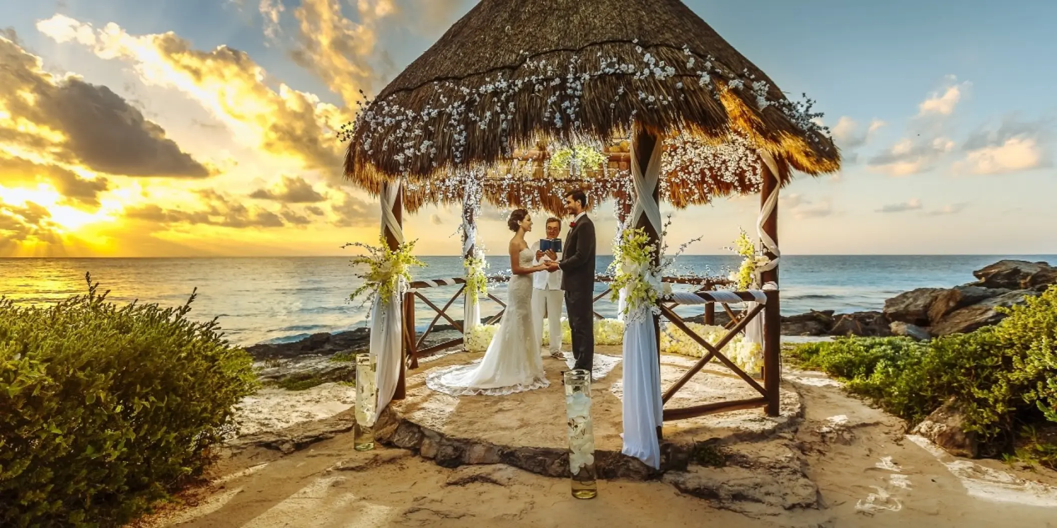 Beachfront wedding ceremony under a thatched gazebo at sunset at Occidental at Xcaret, Playa Del Carmen