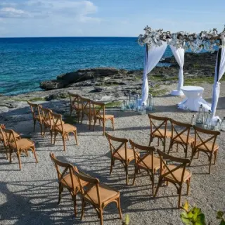 Oceanfront wedding ceremony setup with a white gazebo and wooden chairs at Occidental at Xcaret, Playa Del Carmen