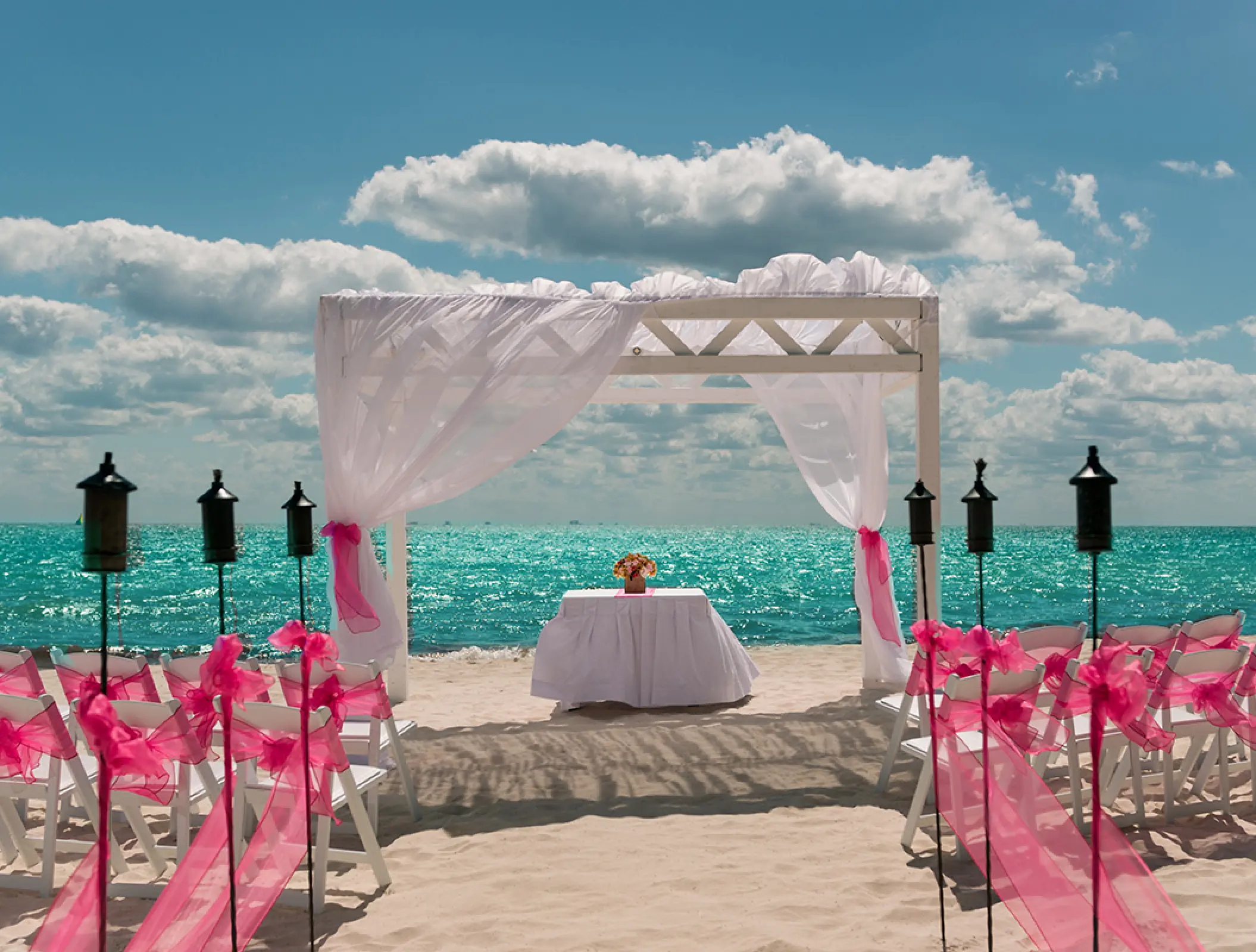 Beachfront wedding ceremony with pink bows and a white arbor at Ocean Coral & Turquesa, Riviera Maya