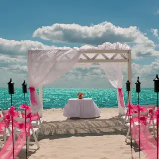 Beachfront wedding ceremony with pink bows and a white arbor at Ocean Coral & Turquesa, Riviera Maya