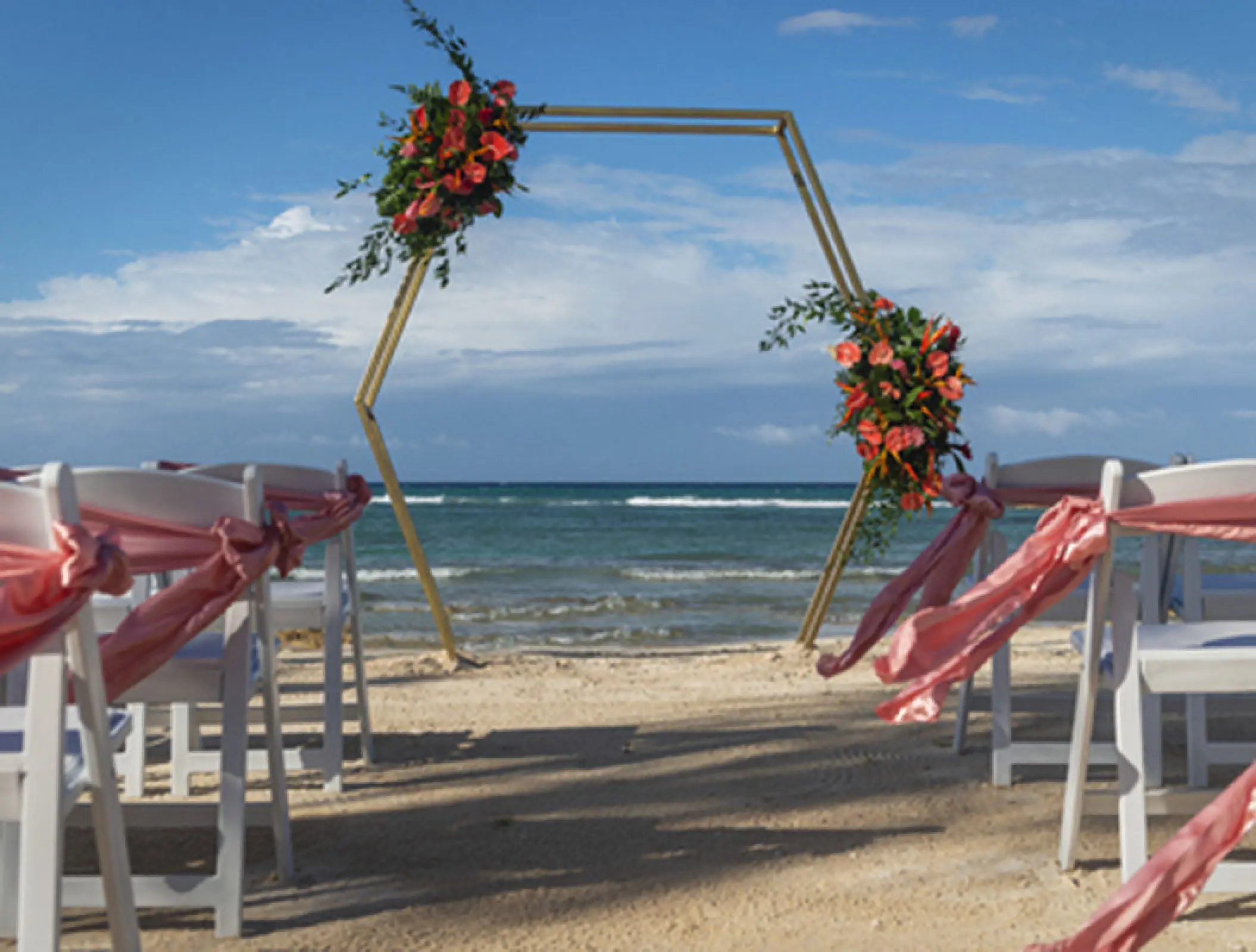 Hexagonal gold wedding arch with red flowers on the beach at Ocean Coral & Turquesa, Riviera Maya