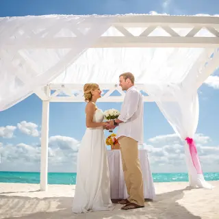 The couple standing under a white gazebo at a beach ceremony at H10 Ocean Coral & Turquesa, Riviera Maya