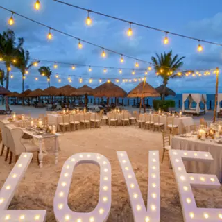 Beachfront wedding reception under string lights with LOVE marquee letters at Ocean Coral & Turquesa, Riviera Maya