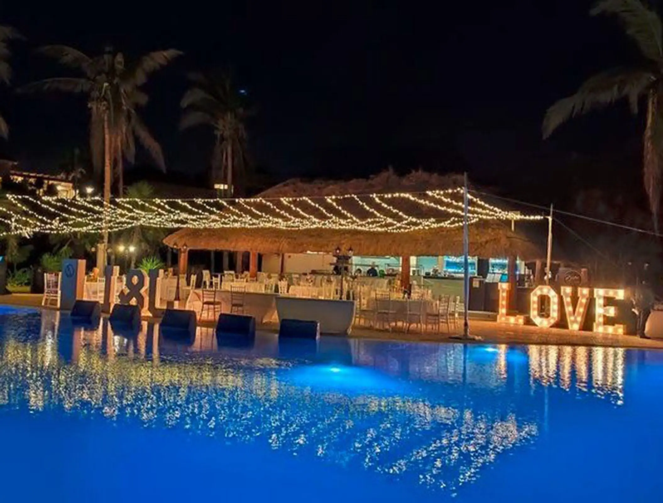 Evening wedding reception terrace with string lights and LOVE marquee sign at Ocean Coral & Turquesa, Riviera Maya