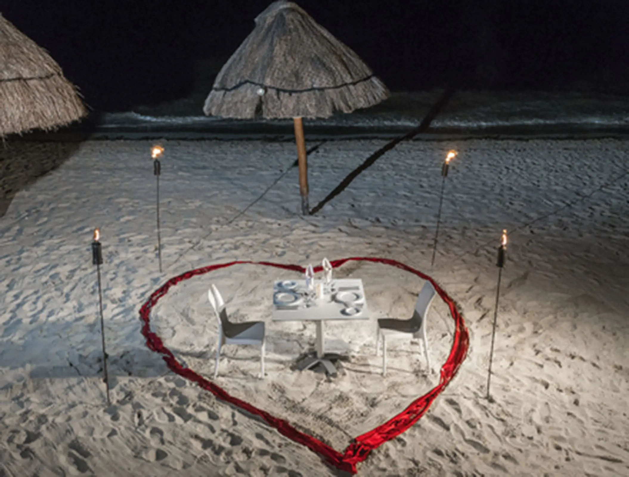 Private beach dinner for two with a heart-shaped red ribbon and torches at H10 Ocean Coral & Turquesa, Riviera Maya
