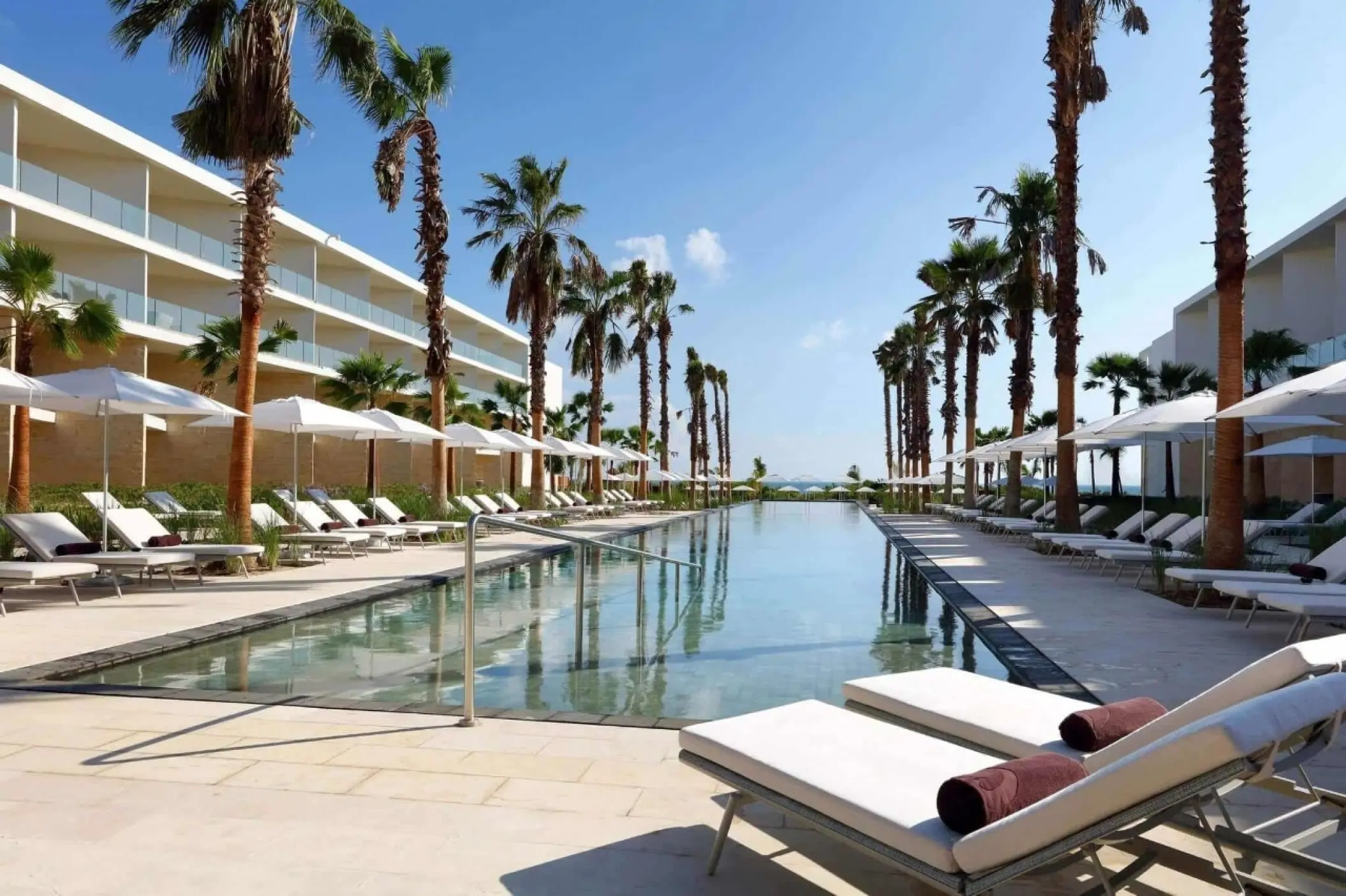 Long lap pool lined with palm trees and white umbrellas at Grand Palladium Costa Mujeres, Cancun