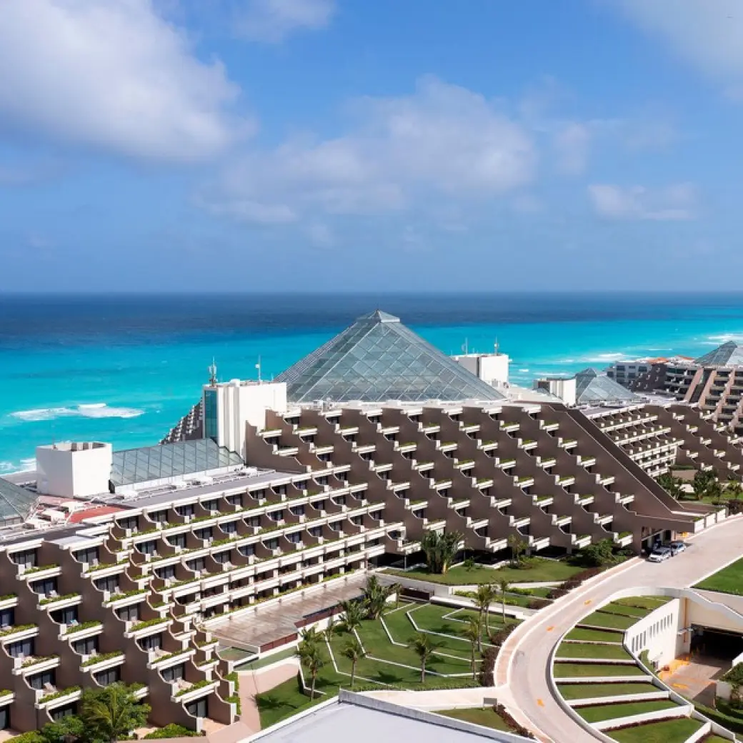 Aerial view of the glass-roofed pyramid buildings at Paradisus Cancun beside turquoise ocean water, Cancun