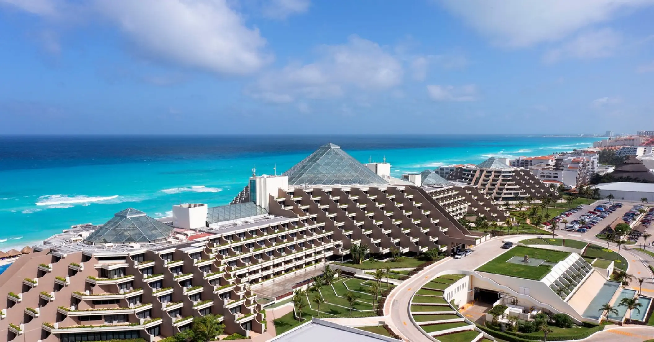 Aerial view of the glass-roofed pyramid buildings at Paradisus Cancun beside turquoise ocean water, Cancun