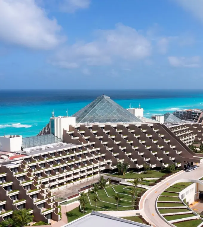 Aerial view of the glass-roofed pyramid buildings at Paradisus Cancun beside turquoise ocean water, Cancun