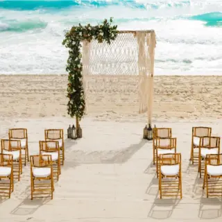 Beachfront wedding ceremony with macrame arch and bamboo chairs at Paradisus Cancun, Cancun