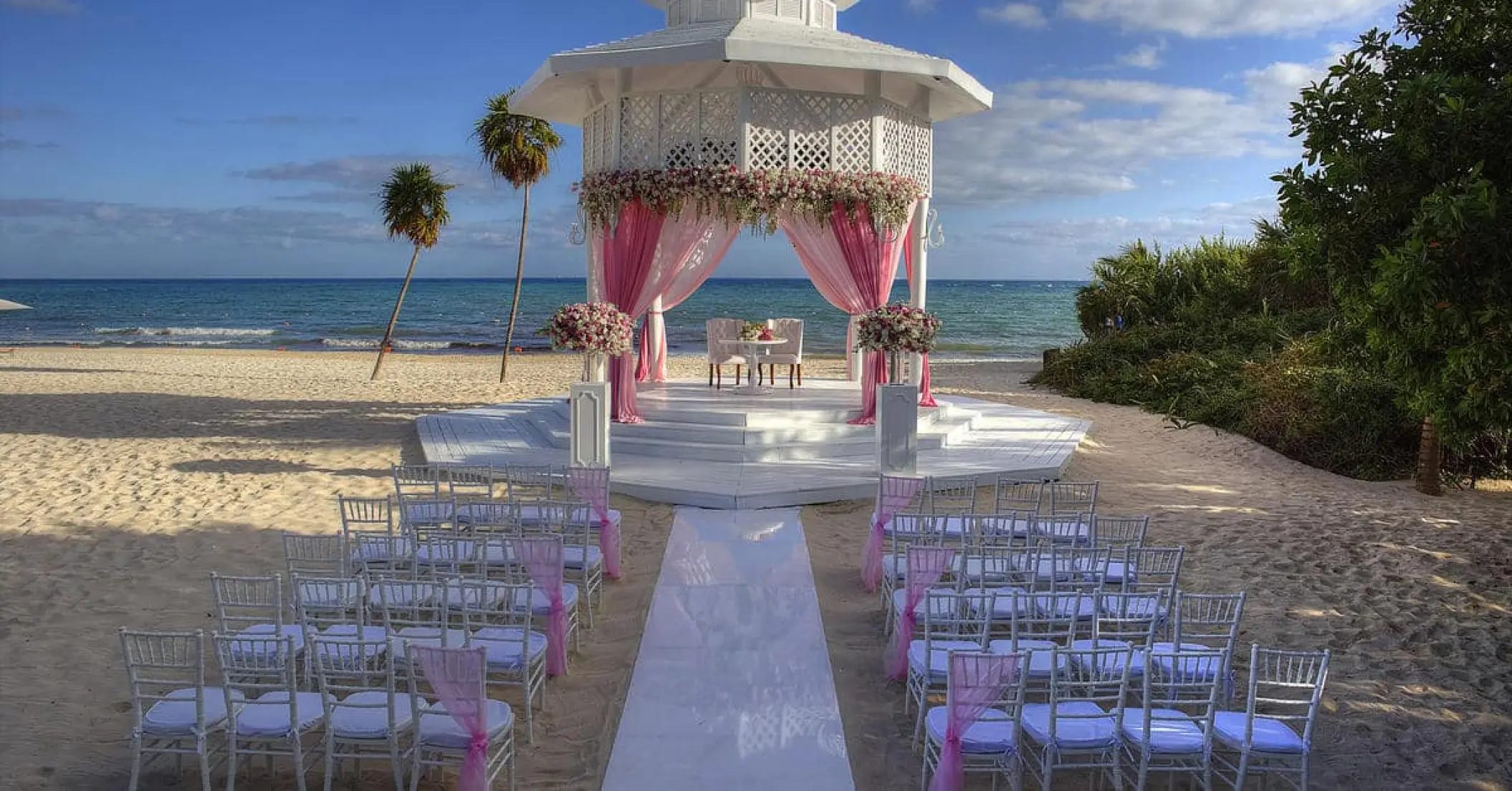 Beachfront wedding ceremony with a white gazebo and pink drapes at Paradisus Playa Del Carmen
