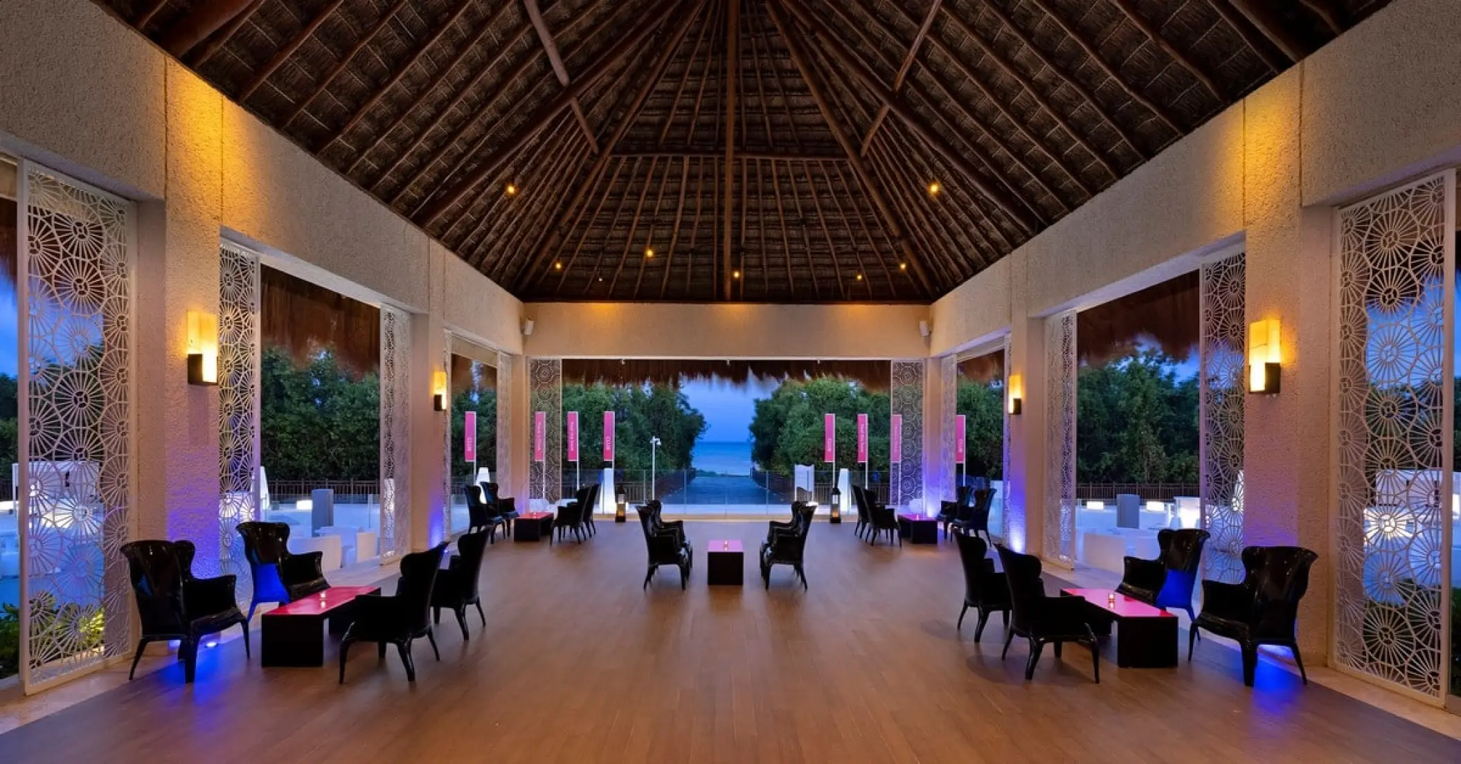 Open-air lounge with a thatched roof and blue lighting at Paradisus Playa Del Carmen
