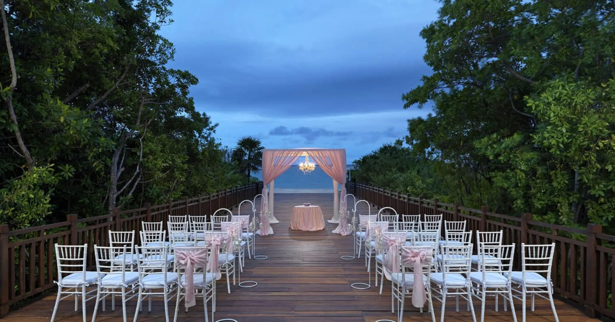 Wooden walkway wedding ceremony with a pink gazebo and white chairs at Paradisus Playa Del Carmen