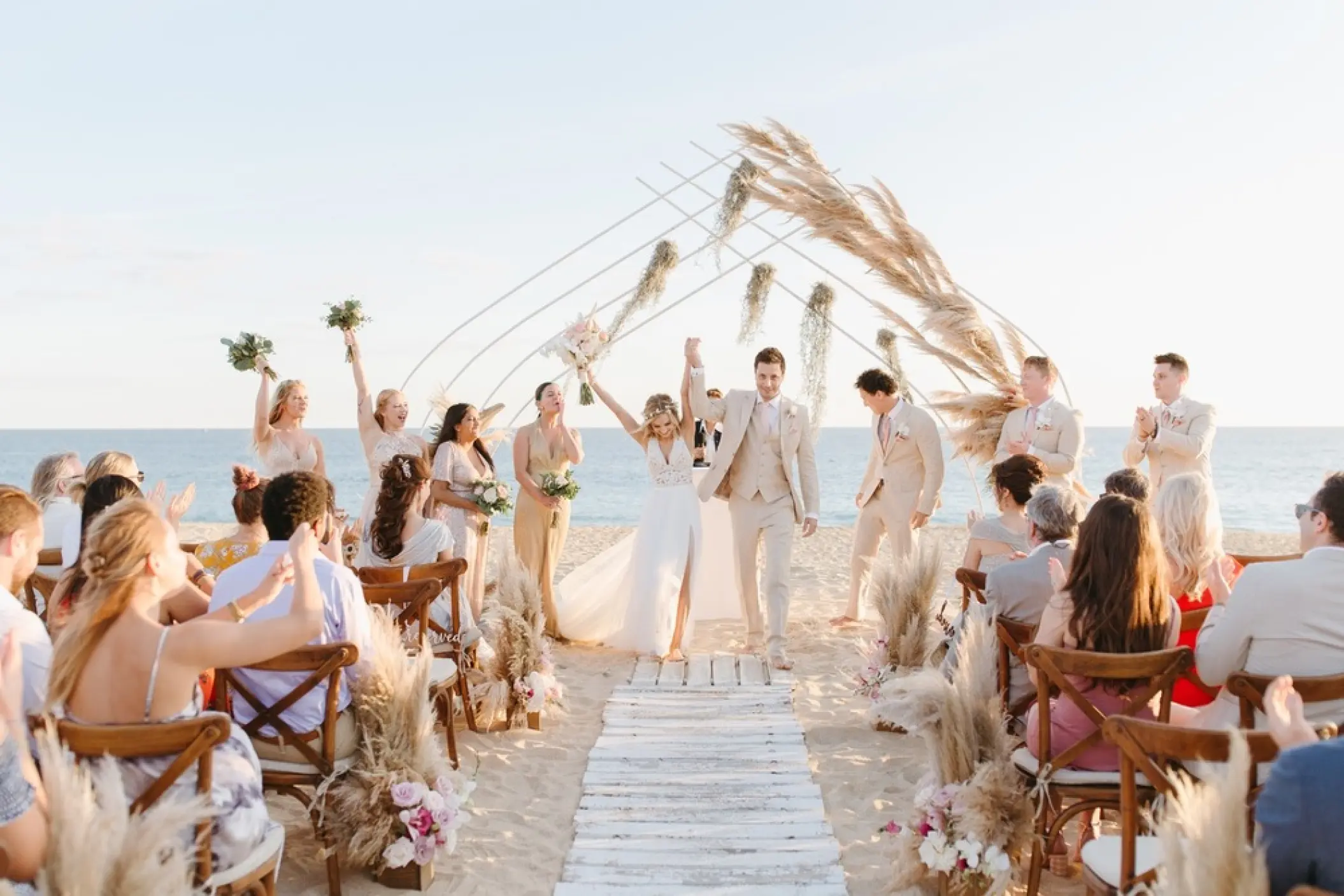 Bride and groom celebrating a beach ceremony under a pampas grass arch at Pueblo Bonito Pacifica, Cabo San Lucas