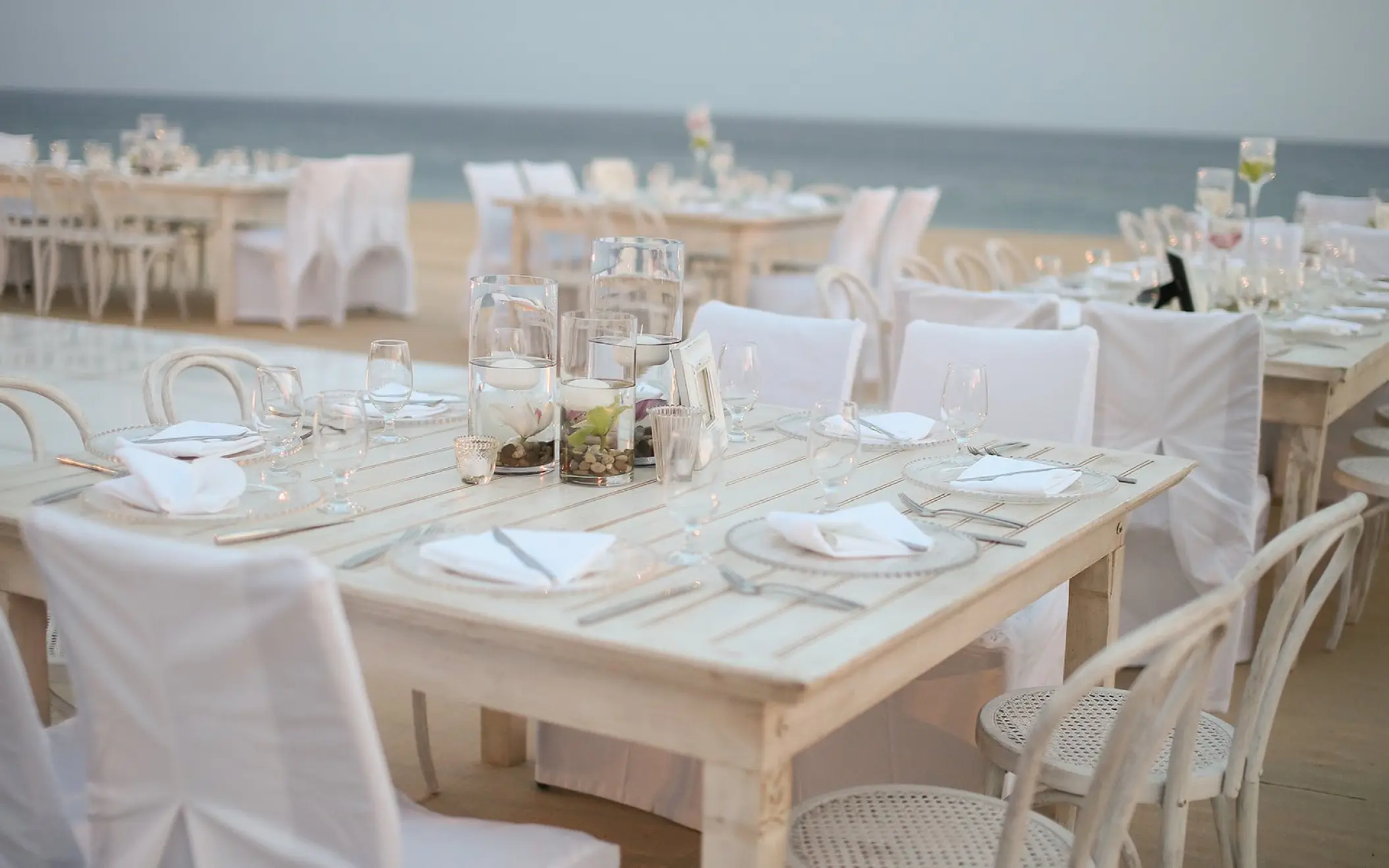 Beachfront wedding reception setup with white wooden tables at Pueblo Bonito Sunset Beach, Cabo San Lucas