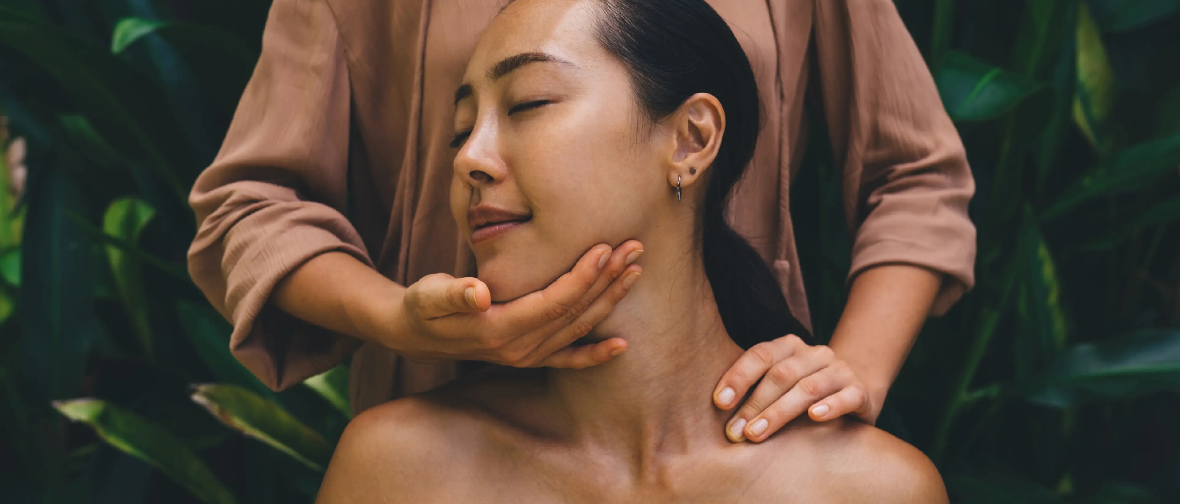 Woman receiving a facial massage during a spa session against a lush tropical leaf background