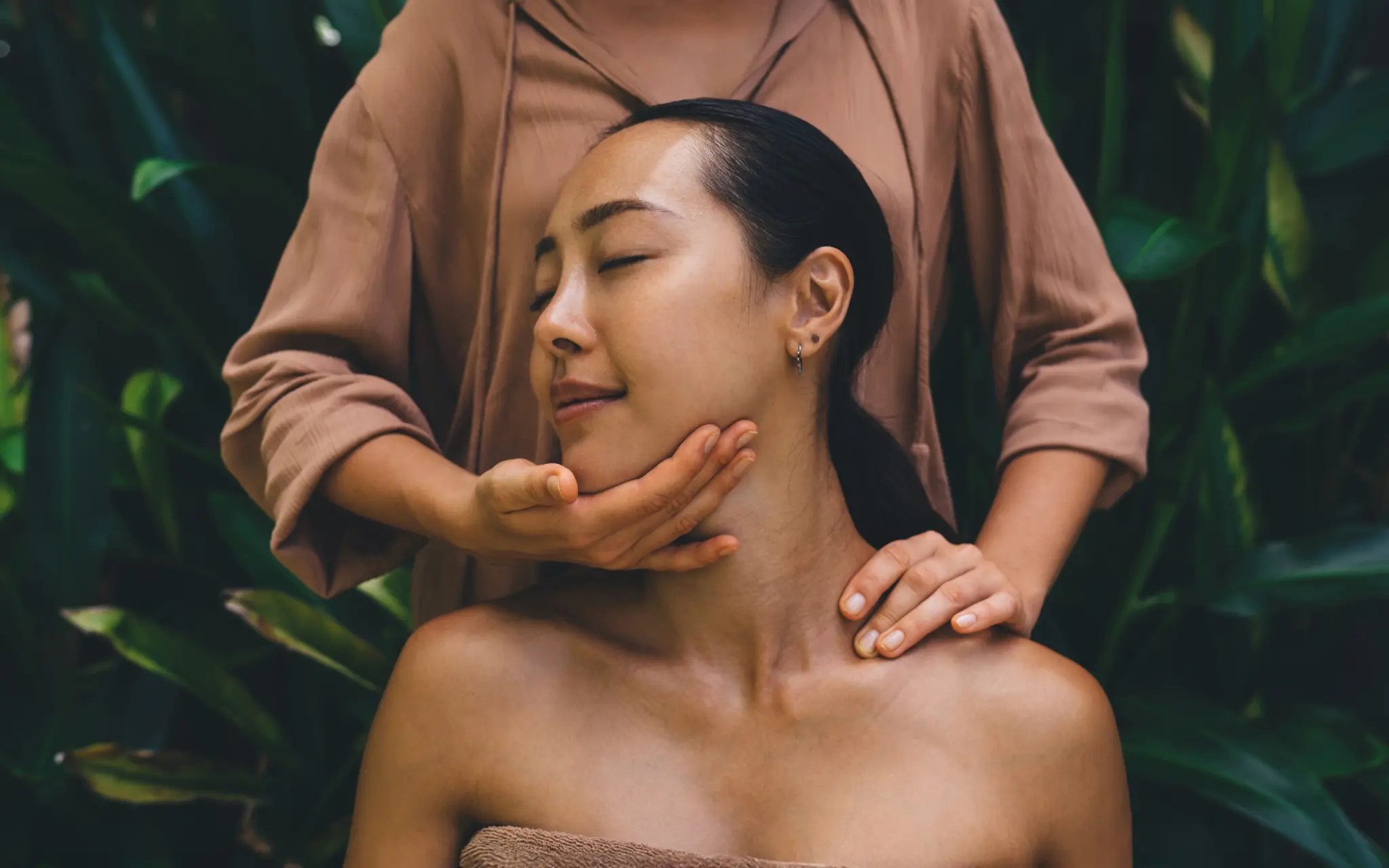 Woman receiving a facial massage during a spa session against a lush tropical leaf background