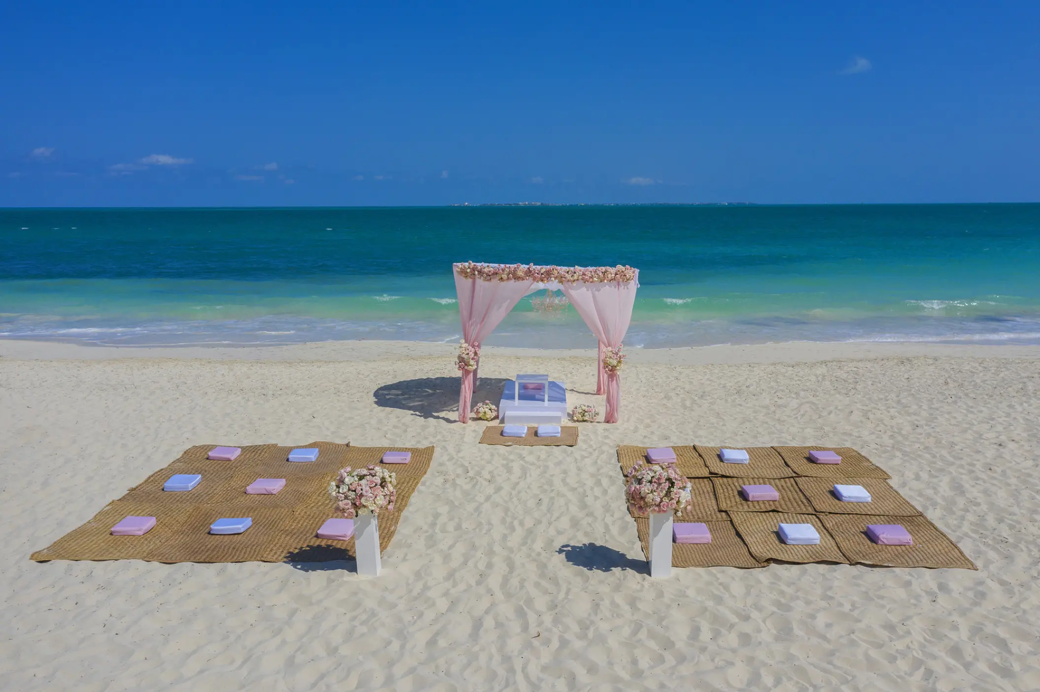 Beach wedding ceremony with pink draped arch and floor cushions at Planet Hollywood Cancun