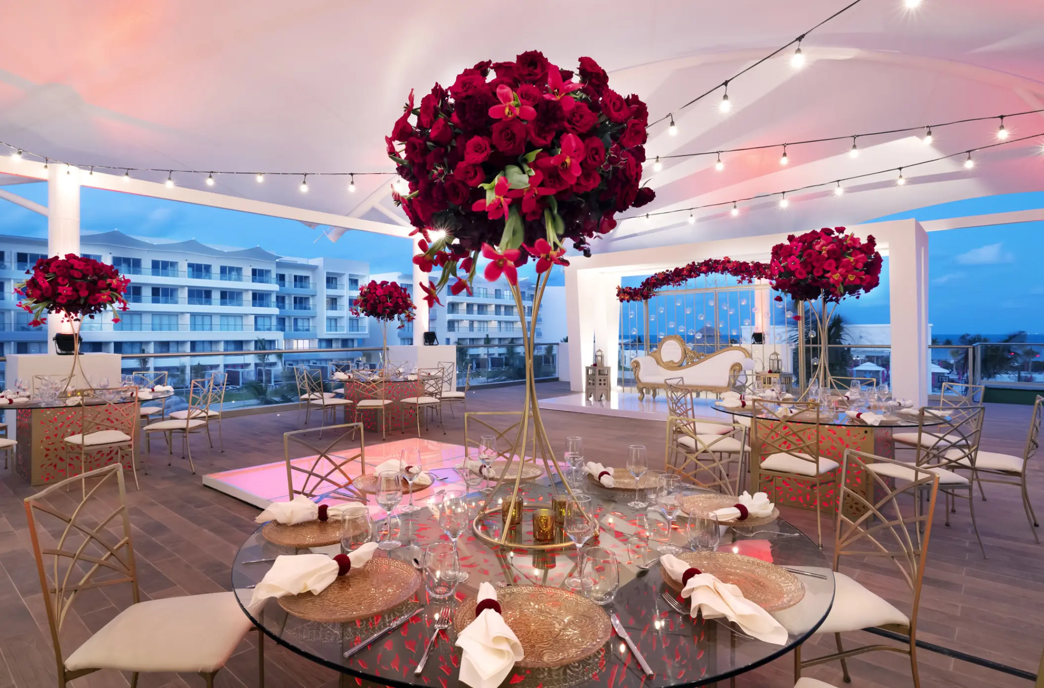 Terrace wedding reception with red floral centerpieces and string lights at Planet Hollywood Cancun