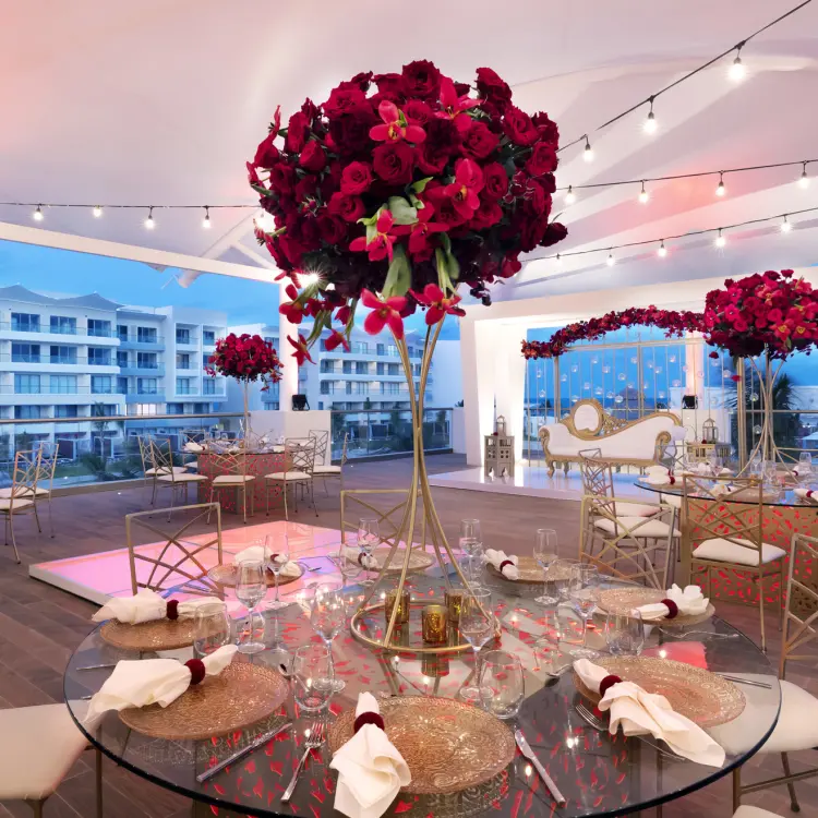 Terrace wedding reception with red floral centerpieces and string lights at Planet Hollywood Cancun