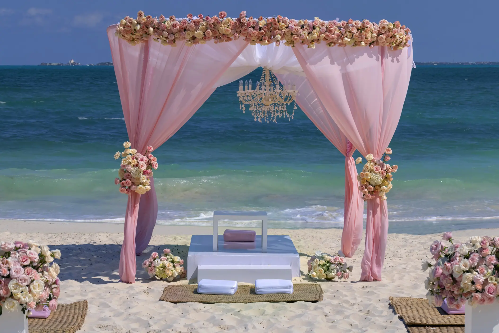 Beachfront wedding ceremony arch with pink draping and a chandelier at Planet Hollywood Cancun