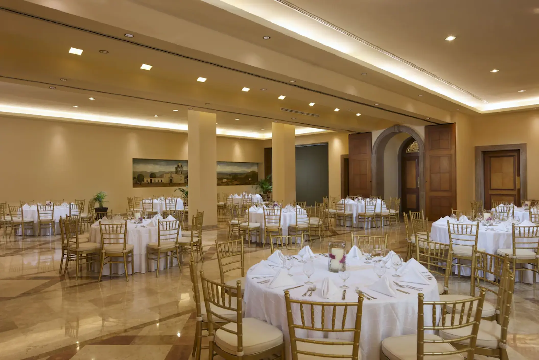 Indoor ballroom wedding reception with round tables and gold chairs at Playa Grande Resort, Cabo San Lucas