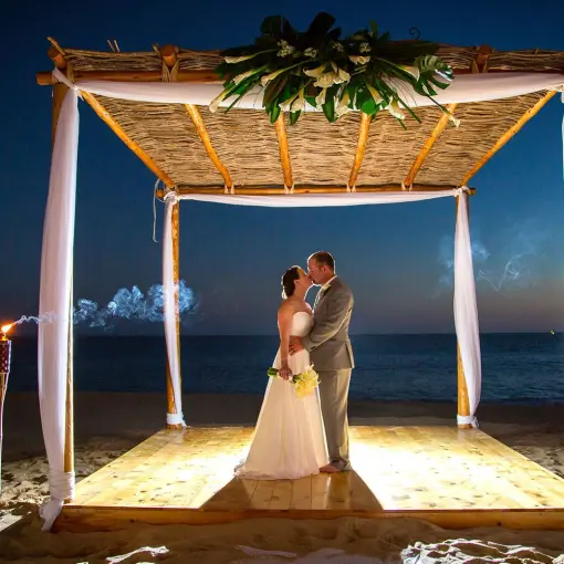 The bride and groom kissing under a bamboo huppah at night at Playa Grande Resort, Cabo San Lucas