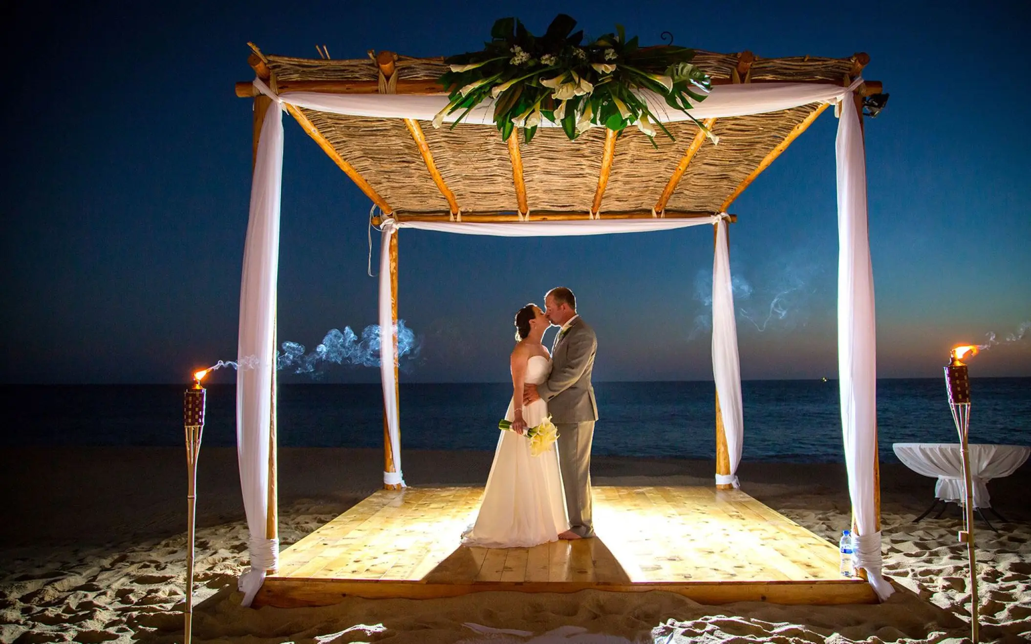 The bride and groom kissing under a bamboo huppah at night at Playa Grande Resort, Cabo San Lucas