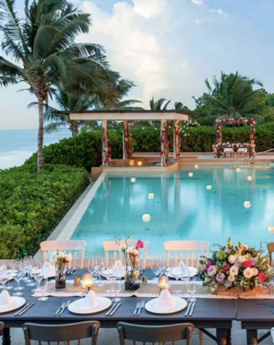 Poolside wedding reception setup with floral arrangements and ocean views in Playa del Carmen