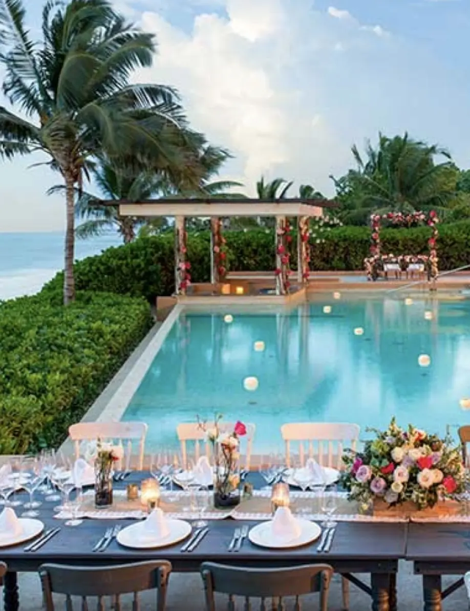 Poolside wedding reception setup with floral arrangements and ocean views in Playa del Carmen