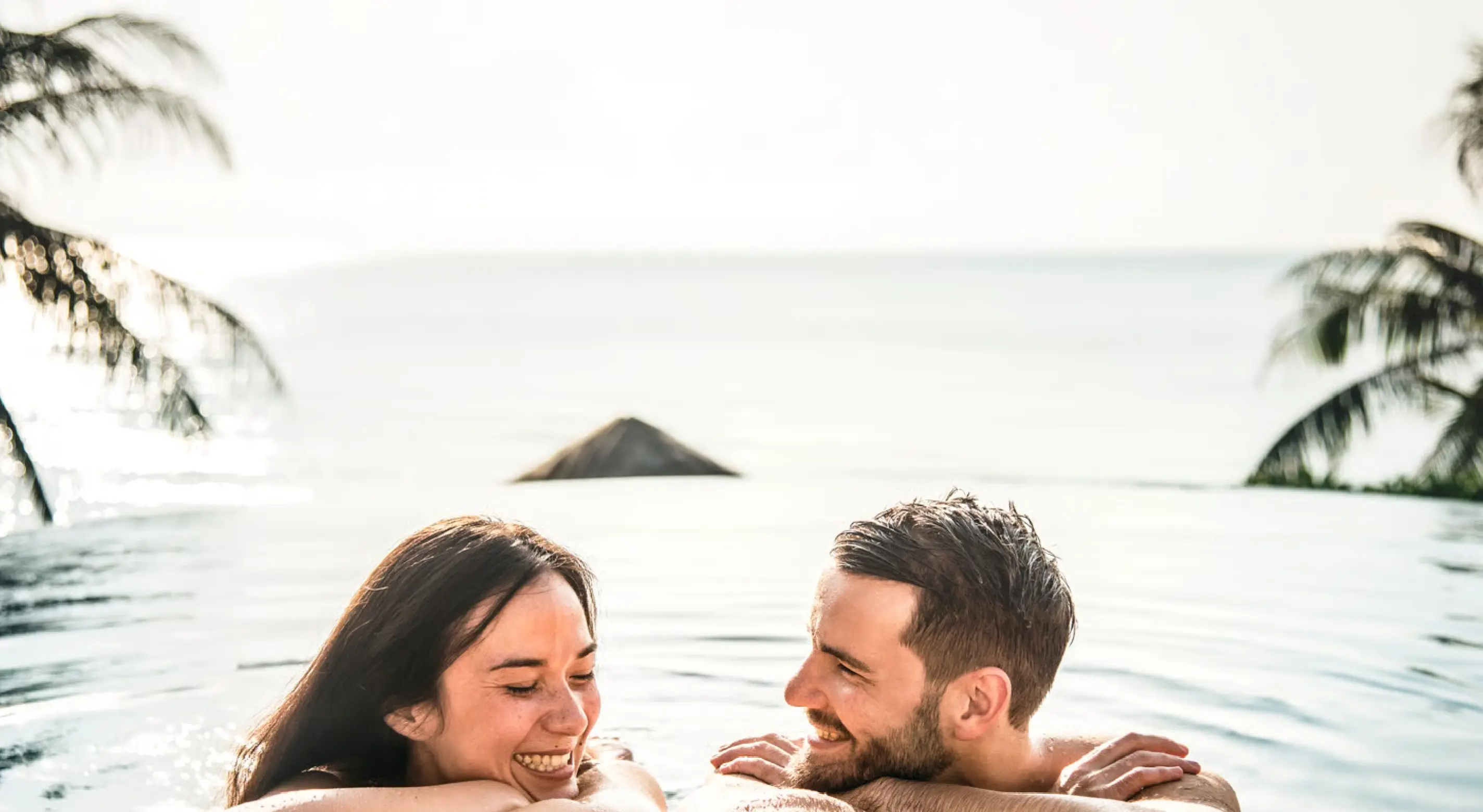 Smiling couple in an infinity pool overlooking the ocean