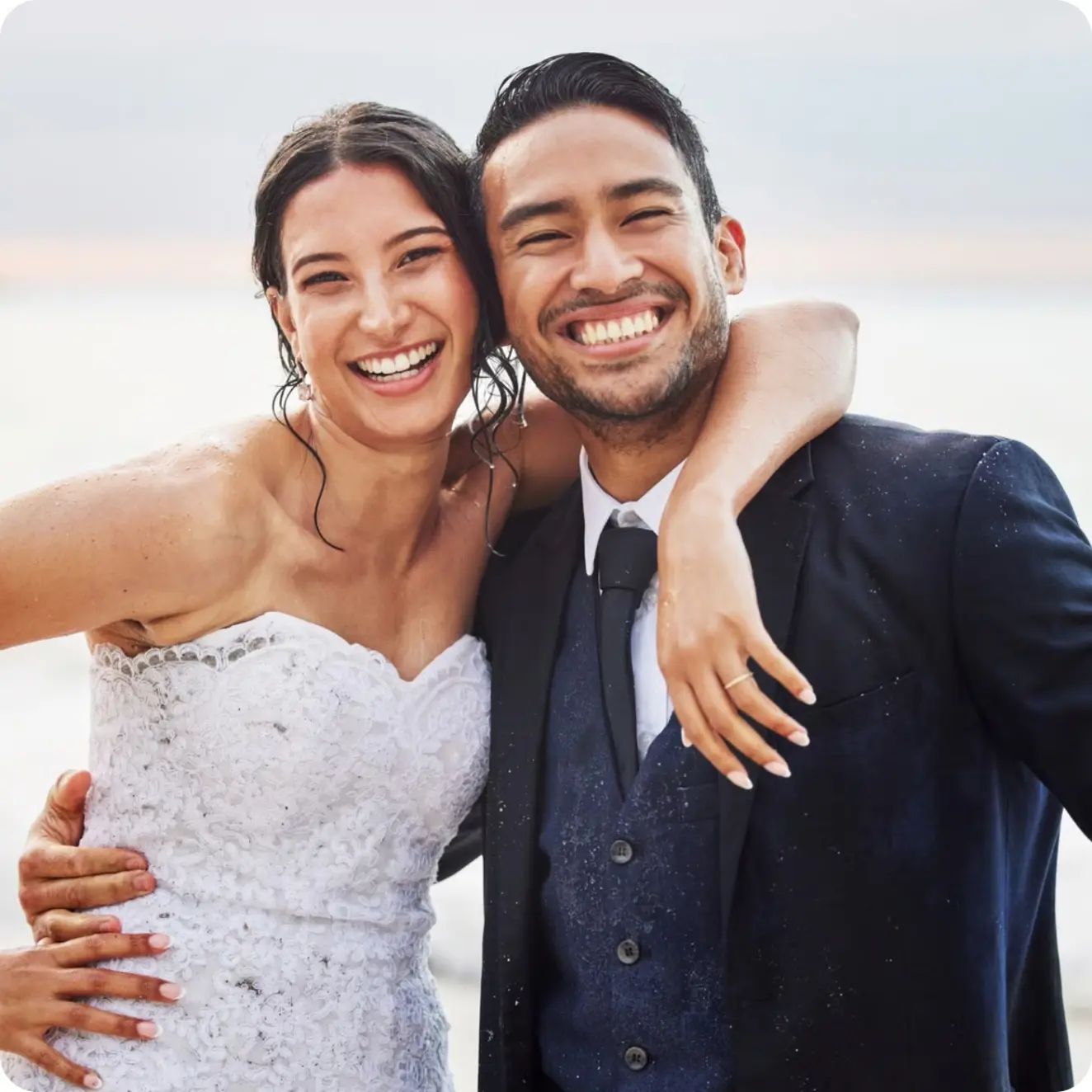 Smiling bride and groom embracing on a beach at sunset