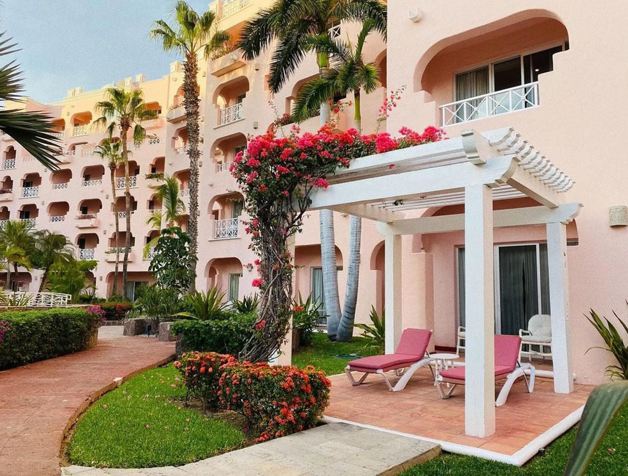 White pergola and pink lounge chairs in the garden at Pueblo Bonito Rose, Cabo San Lucas