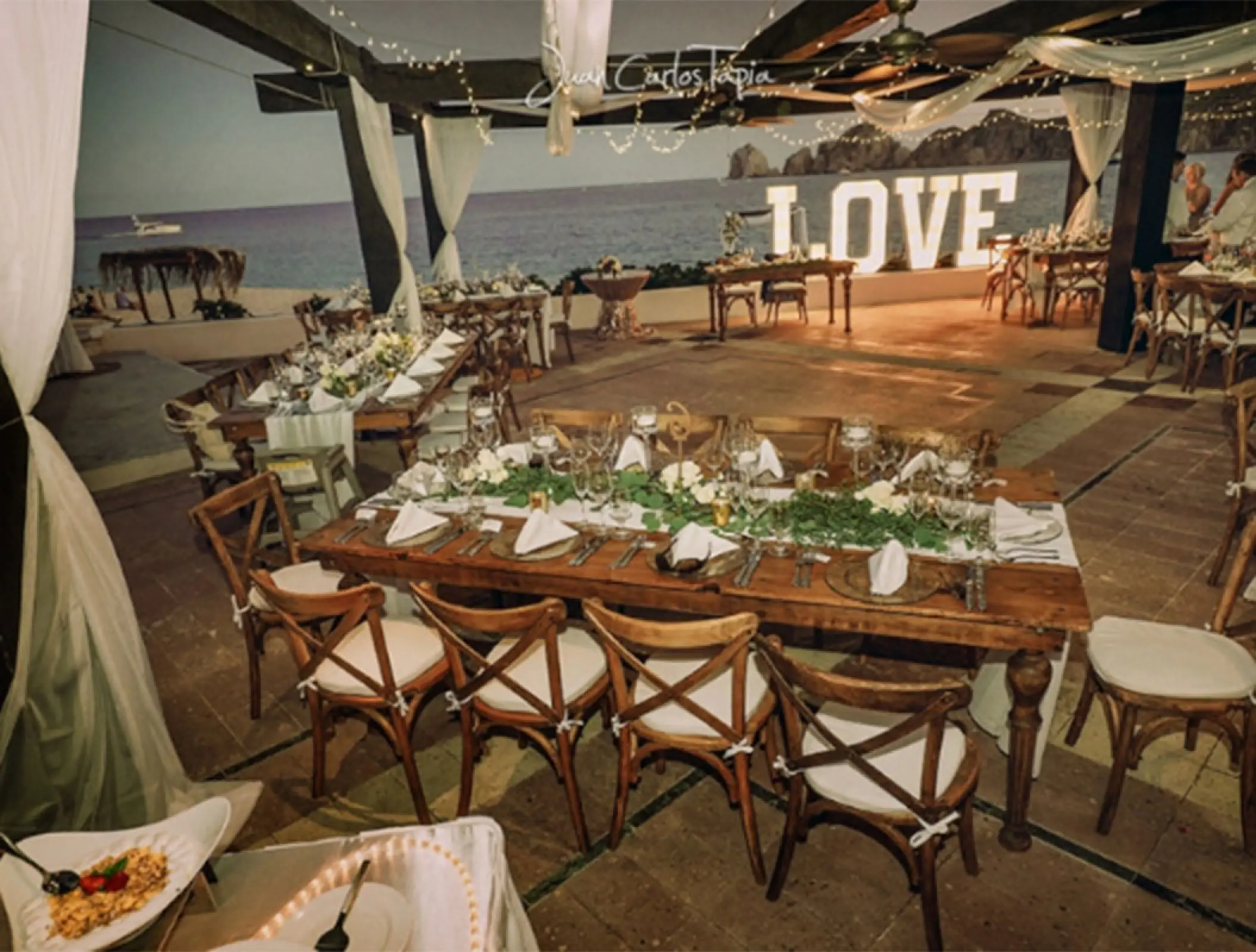 Terrace wedding reception at Pueblo Bonito Rose with wooden tables and a lighted LOVE sign, Cabo San Lucas