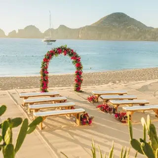 Beachfront wedding ceremony with a floral arch and wooden benches at Pueblo Bonito Rose, Cabo San Lucas