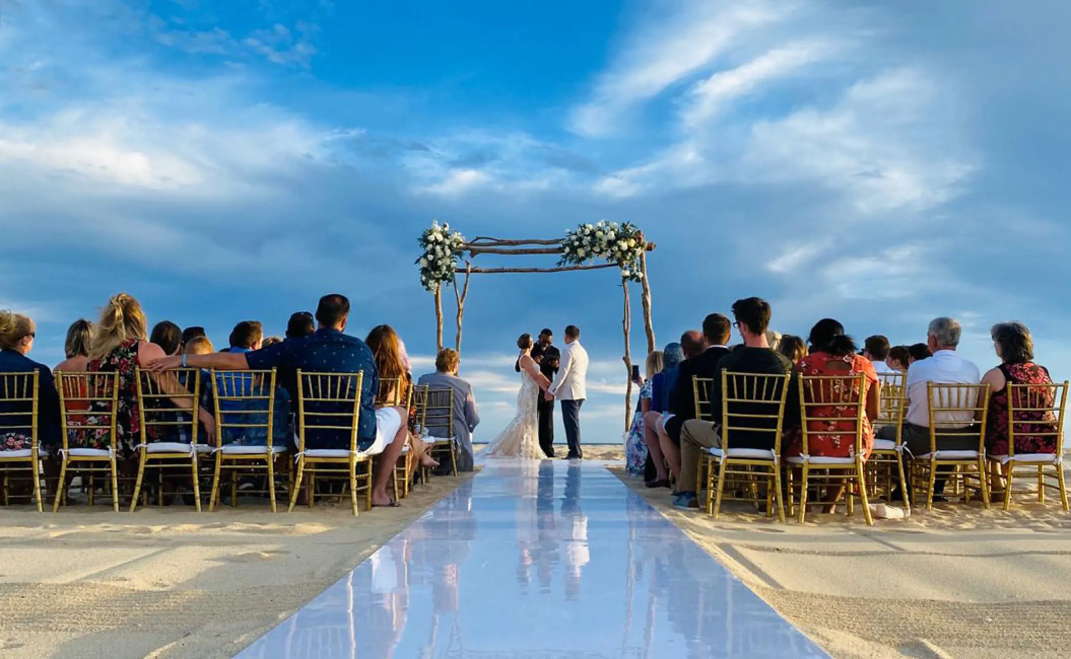 Beachfront wedding ceremony with a white aisle and floral arch at Pueblo Bonito Rose, Cabo San Lucas
