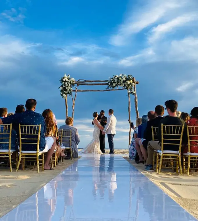Beachfront wedding ceremony with a white aisle and floral arch at Pueblo Bonito Rose, Cabo San Lucas